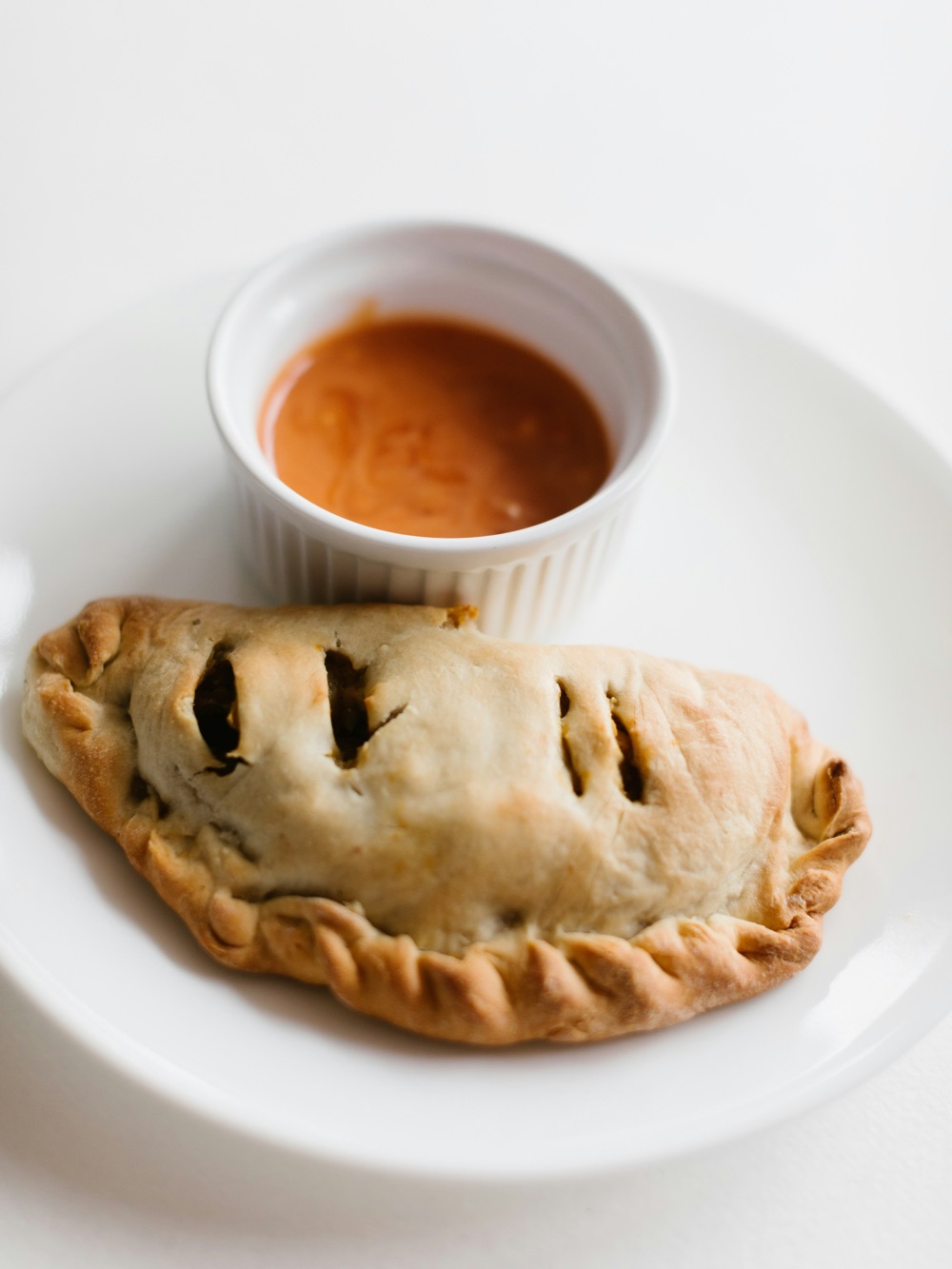 A baked calzone with dipping sauce